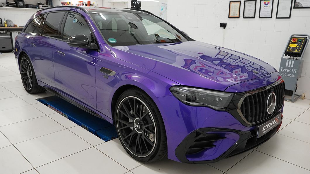 Mercedes E53 AMG in glänzendem violettem Folienfinish steht in einer Werkstatt auf einer Hebebühne