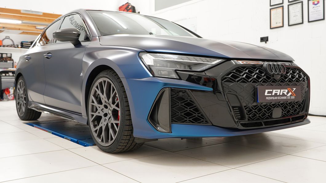 Audi RS3 in mattem Blau-Schwarz steht in einer Werkstatt auf einer Hebebühne, mit markanter Front und großen Felgen