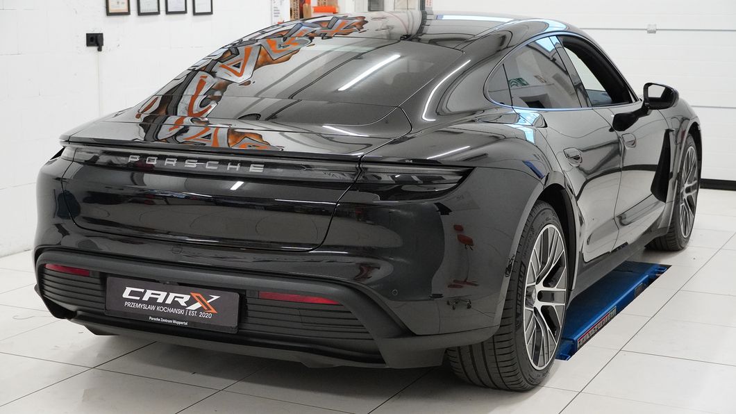 Schrägheckansicht eines schwarzen Porsche Taycan mit stark getönten Scheiben in einer Werkstatt